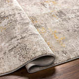 Close-up of the Yuji Area Rug showing its beachhouse, cloud gray, and nutmeg colors and textured, abstract pattern. Fold