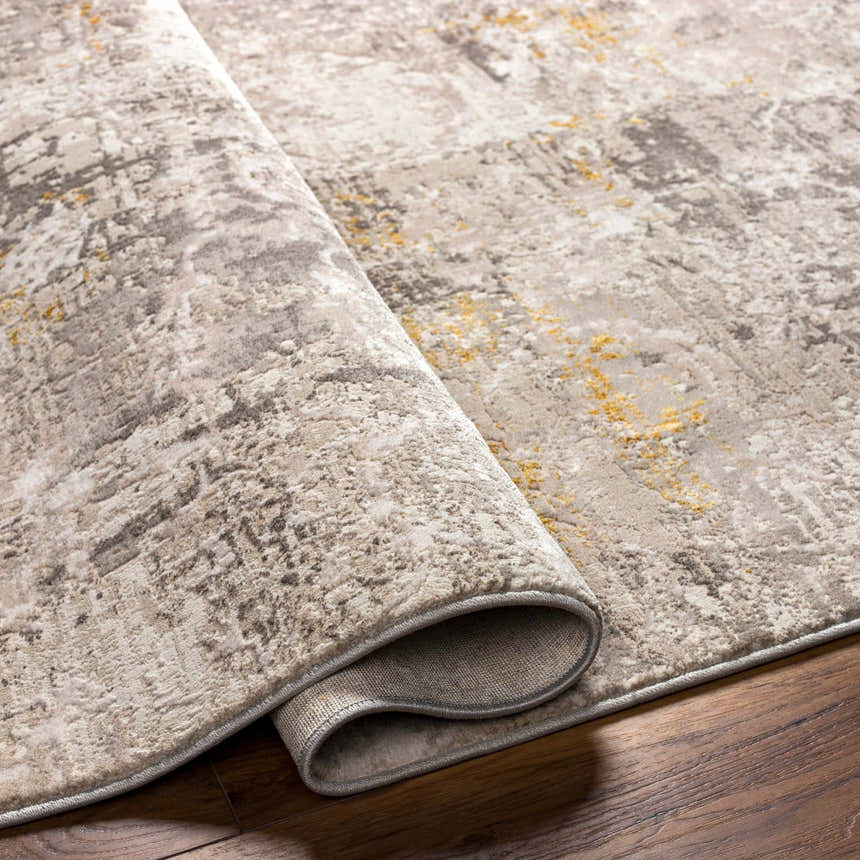 Close-up of the Yuji Area Rug showing its beachhouse, cloud gray, and nutmeg colors and textured, abstract pattern. Fold