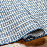 Close-up of the Amena Blue Area Rug showing its woven texture and geometric block pattern in denim and white. Fold
