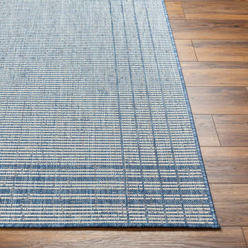 Close-up of the Eneco Blue Area Rug showing its woven texture and linear pattern in denim and light gray on wood flooring. Front