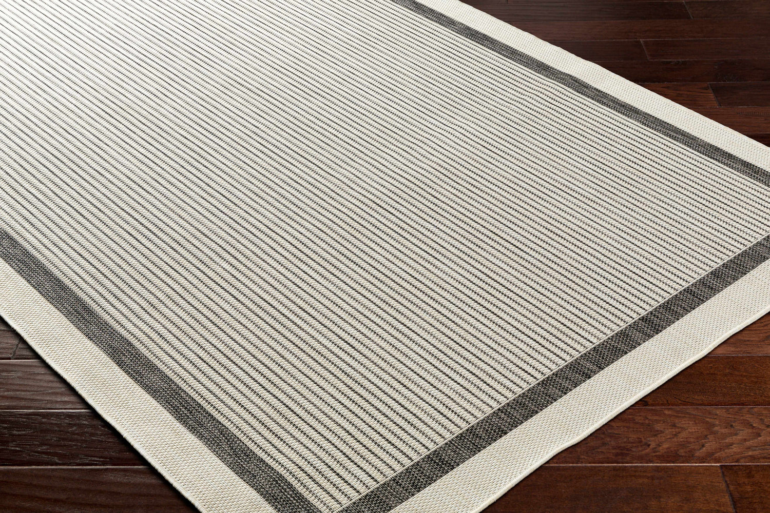 Close up of the Hevel Black & White Area Rug showing its striped pattern and textured weave on a dark wood floor. Corner
