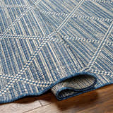 Close-up of the Ivora Blue Area Rug showing its woven texture, denim and natural gray colors, and geometric pattern. Fold