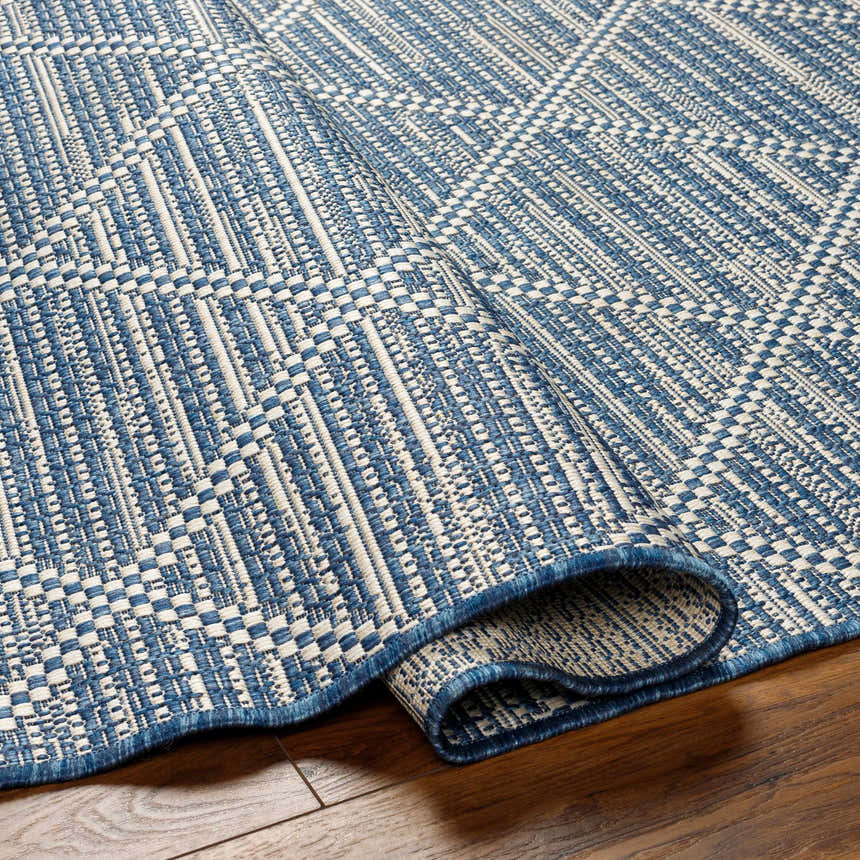 Close-up of the Ivora Blue Area Rug showing its woven texture, denim and natural gray colors, and geometric pattern. Fold