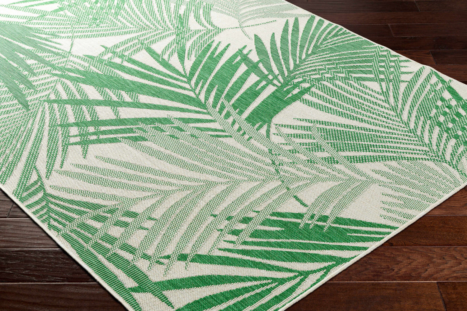 Close up of Jaala Area Rug featuring a green and bone palm leaf design on dark wood flooring. Corner