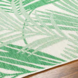 Close-up of the Jaala Area Rug. Beige rug with a light green tropical palm leaf pattern, machine woven texture. Texture