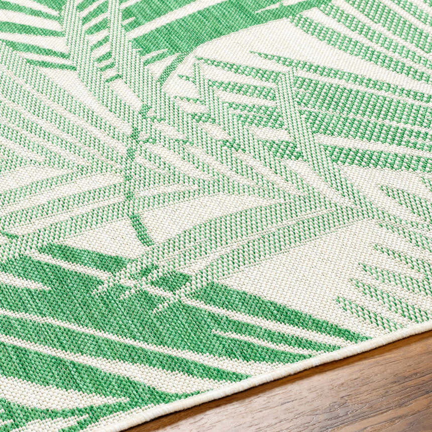 Close-up of the Jaala Area Rug. Beige rug with a light green tropical palm leaf pattern, machine woven texture. Texture