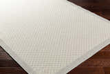 Close-up of the Suzu Area Rug showing a contemporary beige and gray diamond pattern on dark wood floors. Corner
