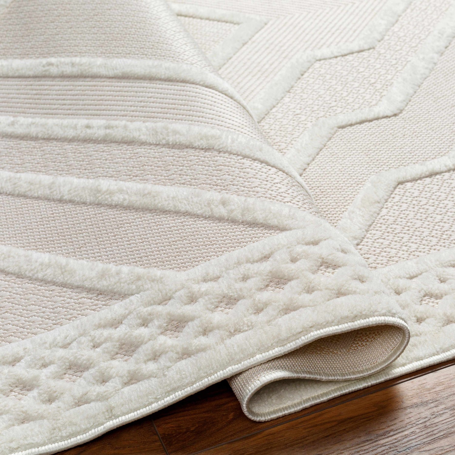 Close-up of the Anja Cream Outdoor Rug showing geometric patterns and soft, textured pile on a wood floor. Fold