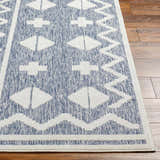 Close-up of Elio Blue Outdoor Rug showing the denim and white geometric pattern and texture on wood flooring. Front