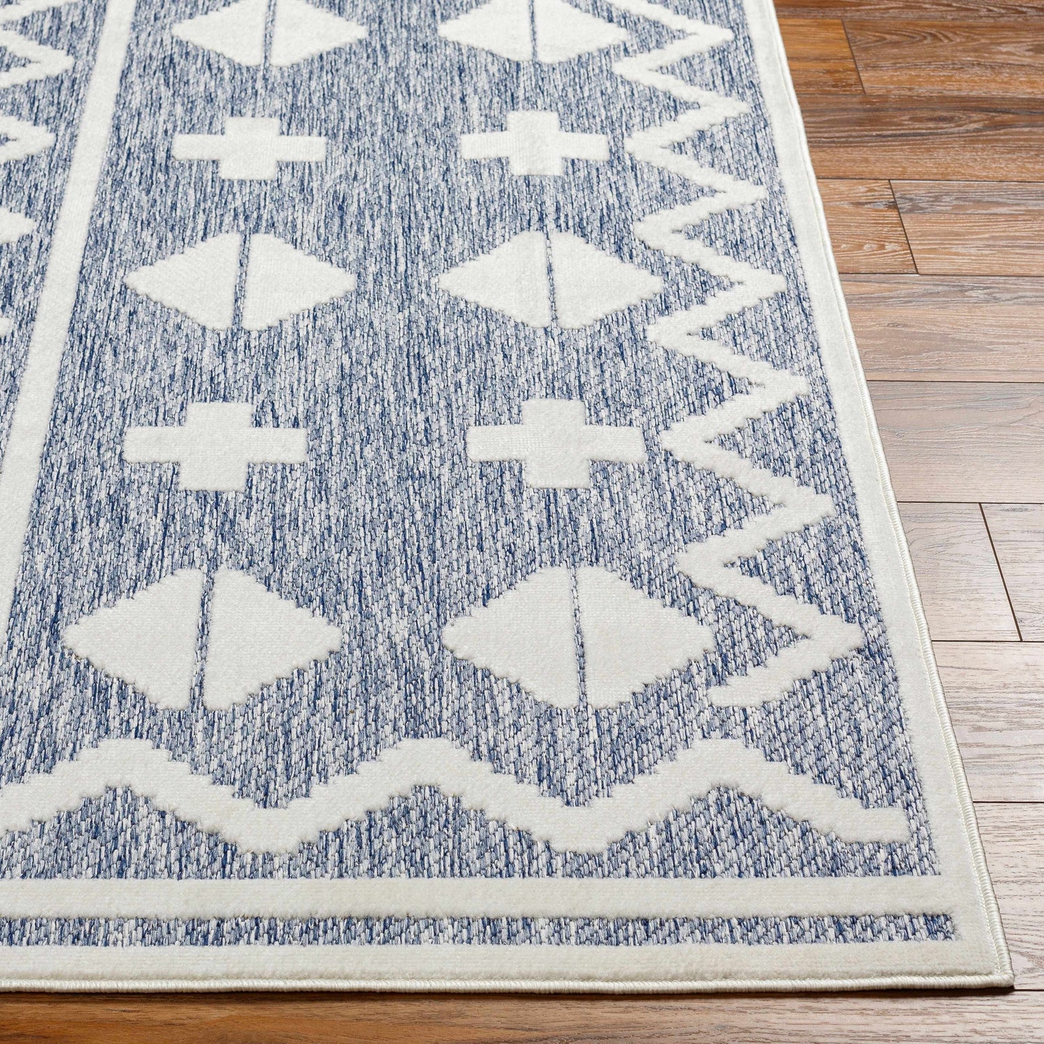 Close-up of Elio Blue Outdoor Rug showing the denim and white geometric pattern and texture on wood flooring. Front