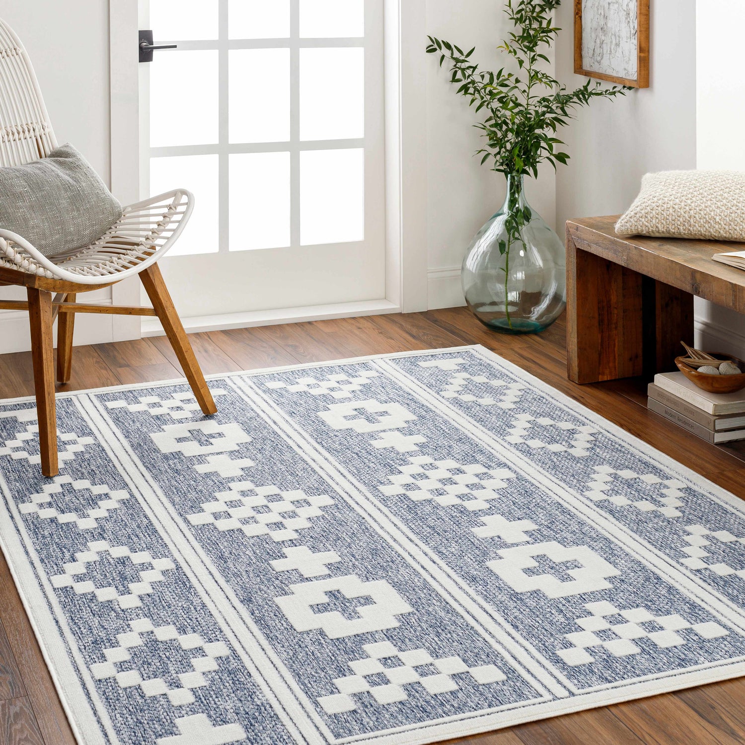 Entryway with Hiro Blue Outdoor Rug, a denim and white geometric rug, white chair, and wooden bench. Roomscene-Rectangle