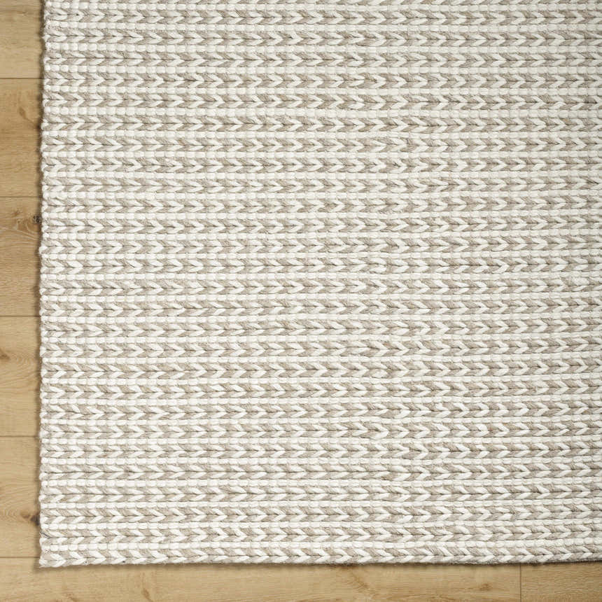 Close-up of the Lenci Hand Woven Wool Area Rug, showcasing beige and rose cream colors and braided texture on wood floor. Corner
