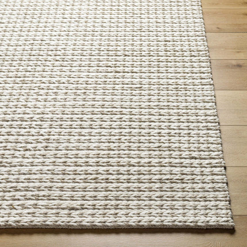 Close-up of the hand woven Lenci Area Rug in beige and rose cream, showing wool texture and braided design on wood floor. Front