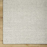 Close up of the hand woven Lenci Bone Area Rug showing beige and bone braided texture on wood floor. Corner