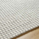 Close up of the hand woven Lenci Bone Area Rug showing its beige and bone braided texture on wood floor. Texture