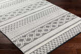 Close-up of the Hala Area Rug, a hand-woven wool rug with geometric patterns in dark gray, nickel, off-white, smoke, and taupe. Corner