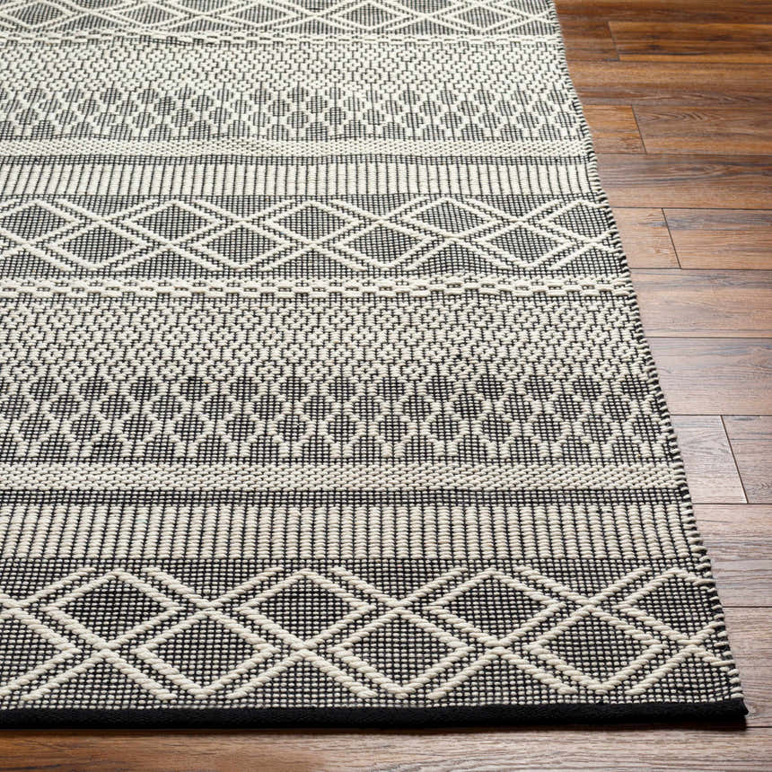 Close-up of the hand woven Hala Area Rug showing its dark gray and off white geometric Scandinavian design and wool texture. Front