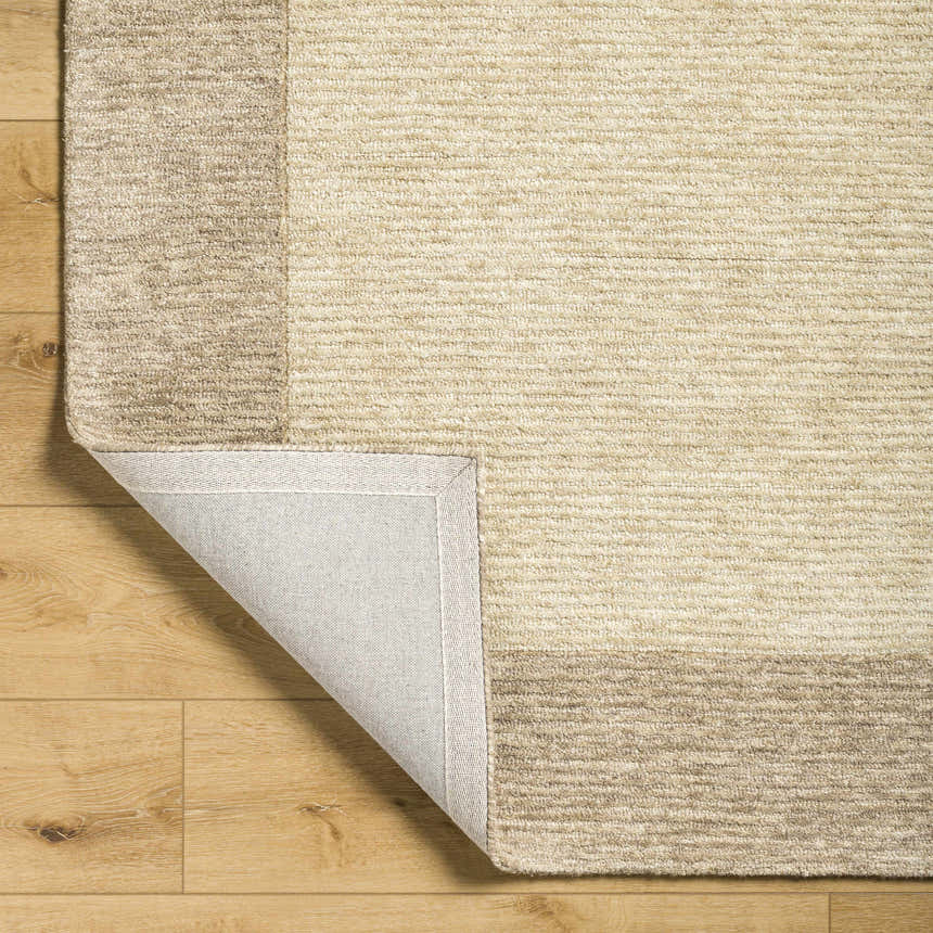 Close-up of the Amadi Area Rug showing its tan and pearl colors, wool texture, and hand-tufted construction. Fold