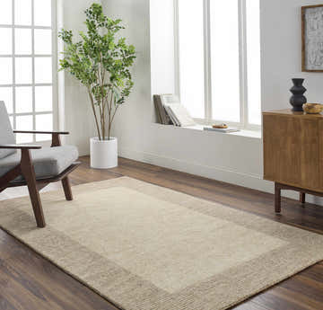 Living room scene with a tan Amadi Area Rug, gray chair, wood cabinet, and large window. Roomscene-Rectangle
