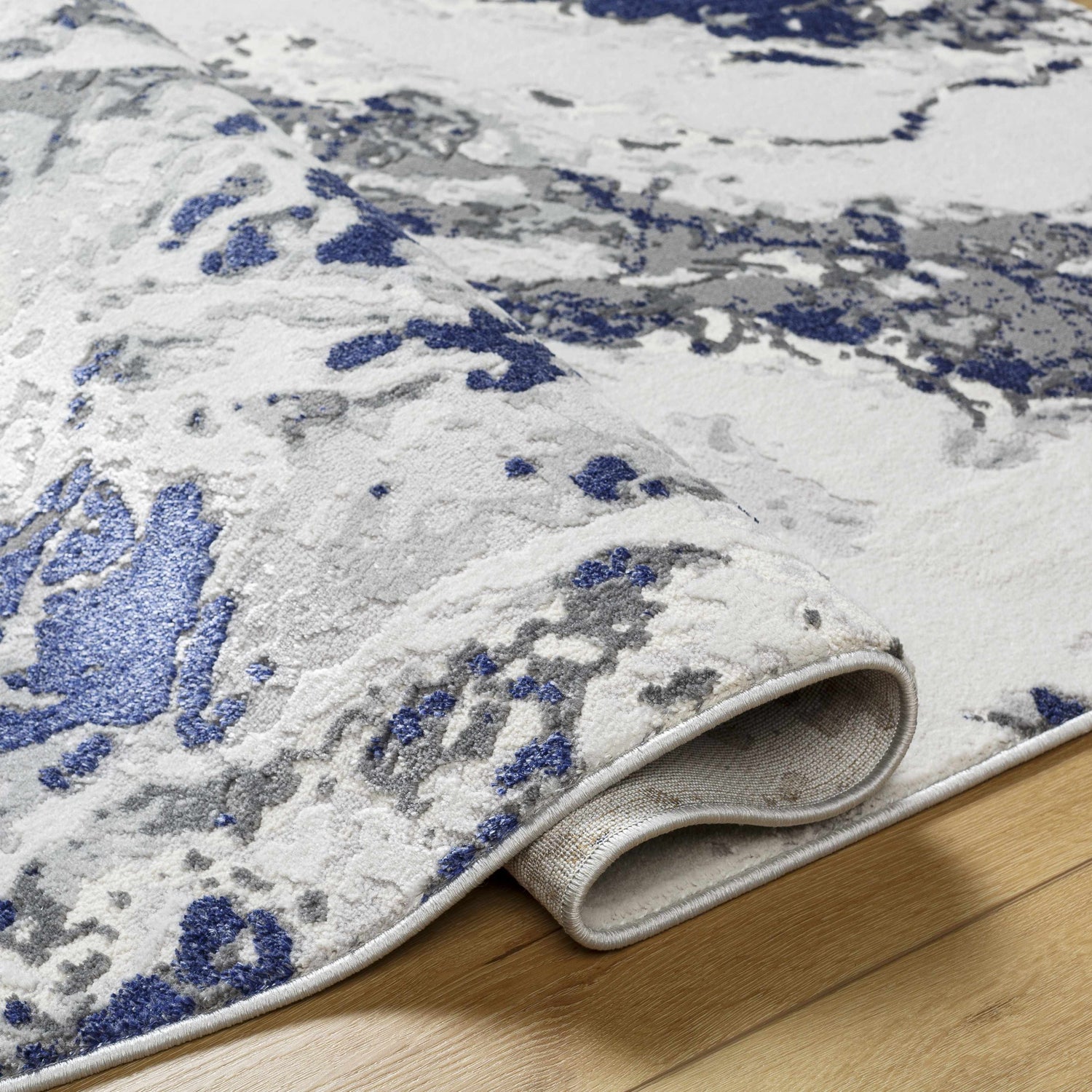 Close-up of the Kaleo Gray & Blue Marble Area Rug showing its abstract pattern, colors, and machine-woven construction. Fold