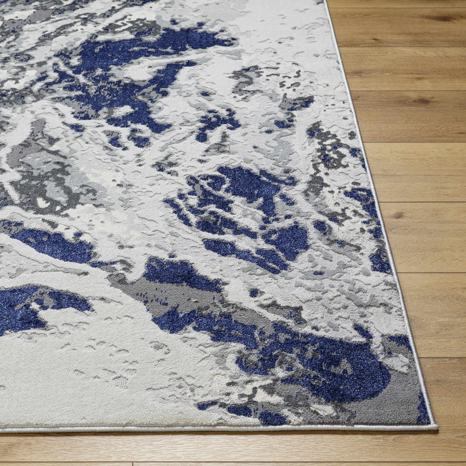 Close up of the Kaleo Gray & Blue Marble Area Rug showing its abstract pattern and soft texture on a wood floor. Front