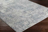 Close-up of Statham Area Rug in charcoal, denim, and ivory on a dark wood floor. Vintage style, machine woven. Corner
