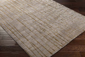 Close-up of the hand-knotted Stetson Area Rug. Features a gray base with a gold geometric pattern on dark wood floors. Corner