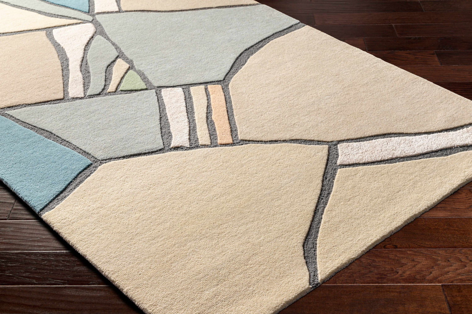 Close-up of the Ashok Area Rug featuring a geometric pattern in beige, bone, and gray tones on dark wood floors. Corner