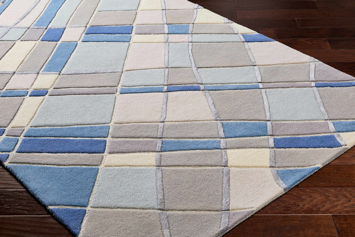 Close-up of the Carla Area Rug, a hand-tufted wool rug with a contemporary geometric block design in blues, grays, and natural tones. Corner