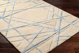 Close-up of Hiba Area Rug. Beige wool rug with a geometric slate blue line pattern. Hand-tufted texture. Corner