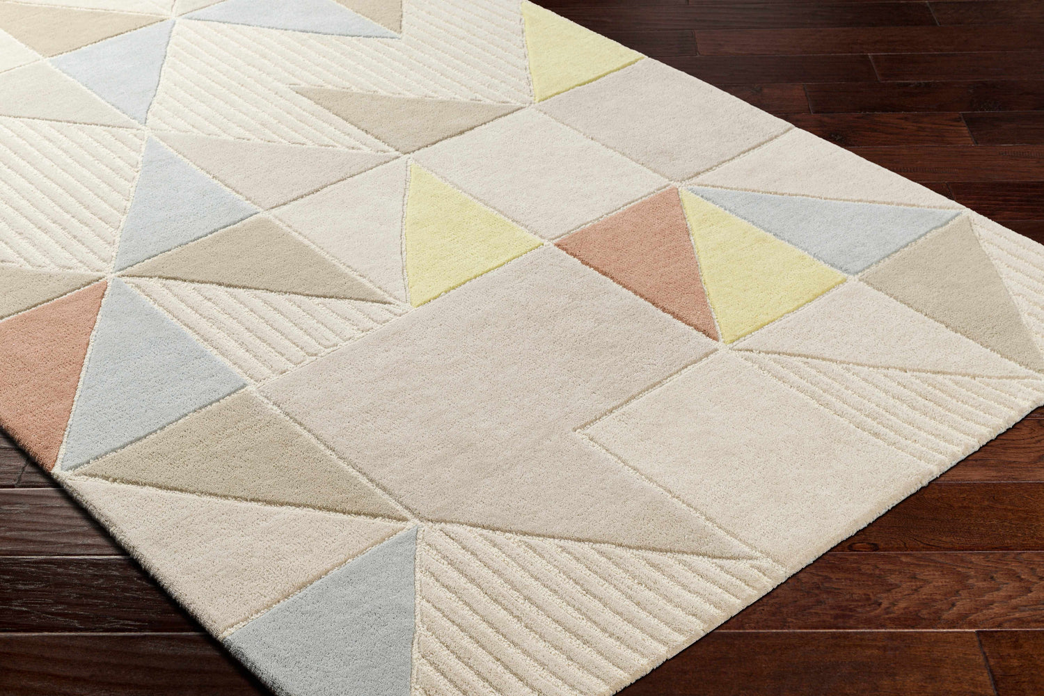 Close-up of Mani Area Rug with geometric triangle pattern in camel, beige, gray, and oatmeal on dark wood floor. Corner