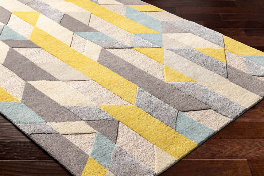 Close-up of the hand-tufted Zoie Area Rug. Features a geometric pattern in camel, gray, lambswool, and saffron hues. Corner