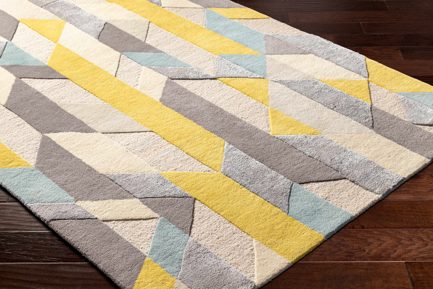 Close-up of the hand-tufted Zoie Area Rug. Features a geometric pattern in camel, gray, lambswool, and saffron hues. Corner