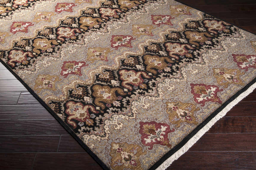 Close-up of the Stoutsville Carpet. Hand-knotted wool rug in amber, black, brick red, and ivory on dark wood floors. Corner