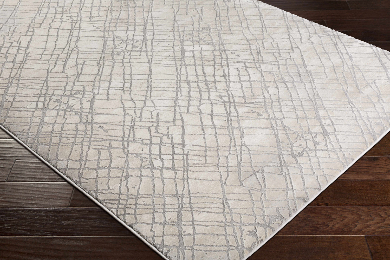 Close-up of the Strykersville Area Rug, a beige rug with a charcoal grid pattern, on dark wood flooring. Corner