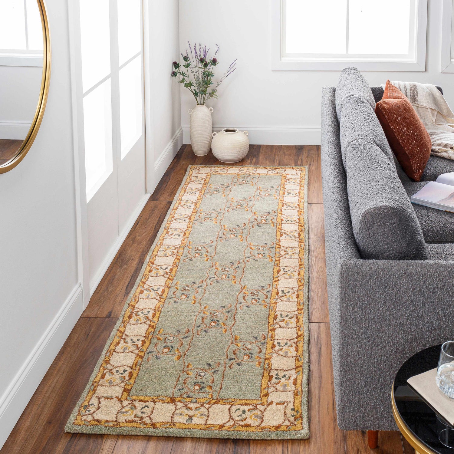 Living room scene with a sage green Stringer Area Rug, gray sofa, wood floors, and natural light. Roomscene-Runner
