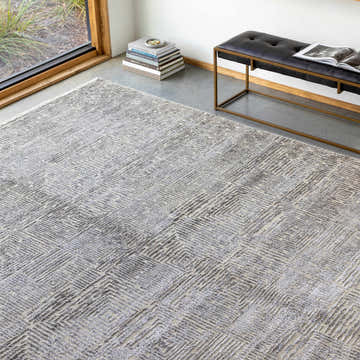 Modern living room scene with gray Struie Area Rug, leather bench, and natural light from a large window. Roomscene-Rectangle