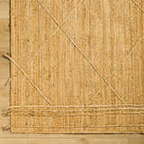 Close-up of hand woven Zeno Area Rug. Tan jute rug with braided detail and natural texture. Corner