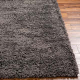 Close-up of the Black Allon Area Rug showing its plush, gray shag texture against wood flooring. Front