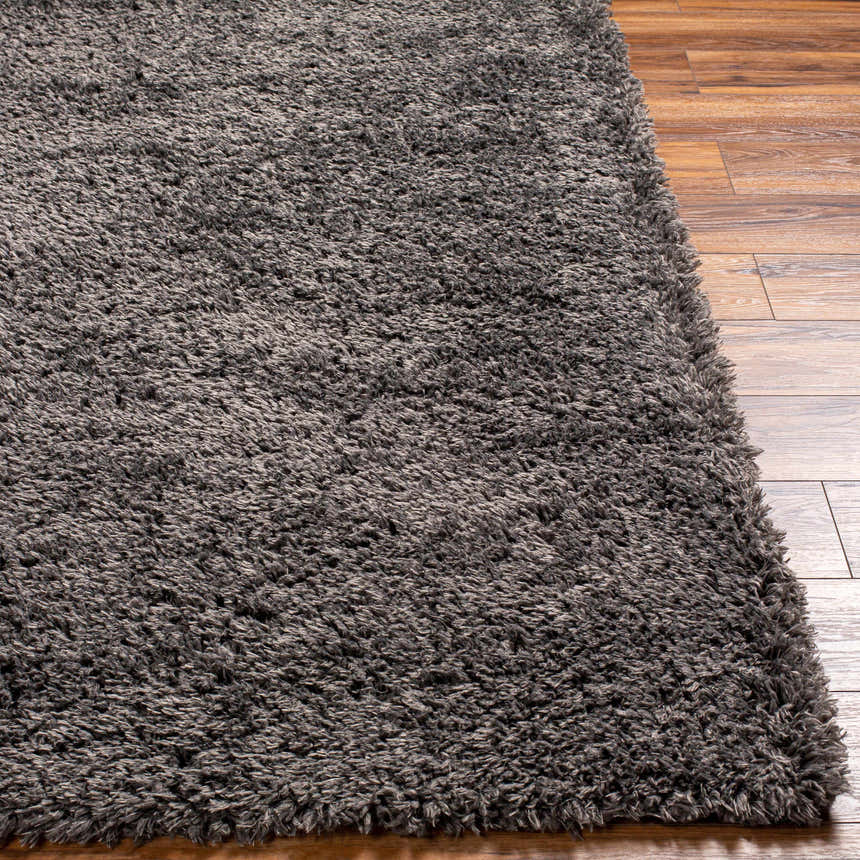 Close-up of the Black Allon Area Rug showing its plush, gray shag texture against wood flooring. Front
