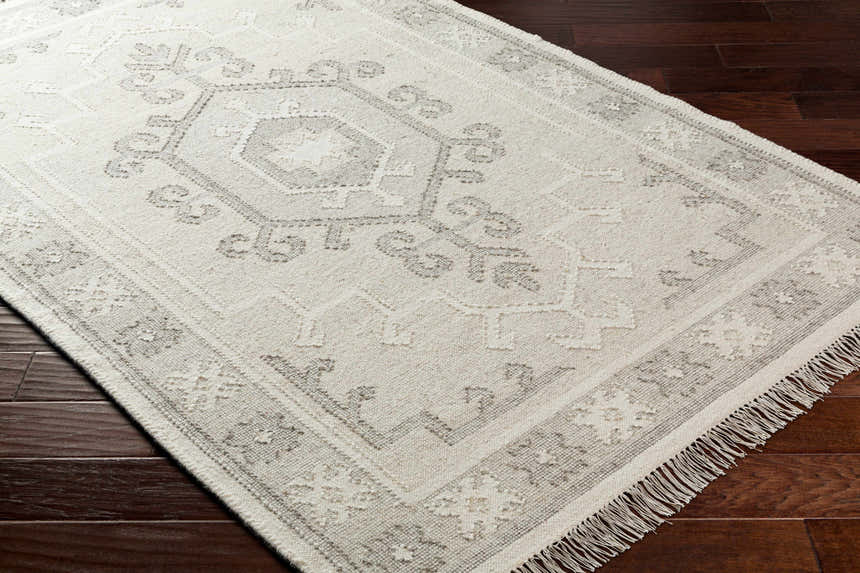 Close-up of the hand woven Afra Area Rug in cloud gray and dark gray with a traditional farmhouse pattern and fringe. Corner