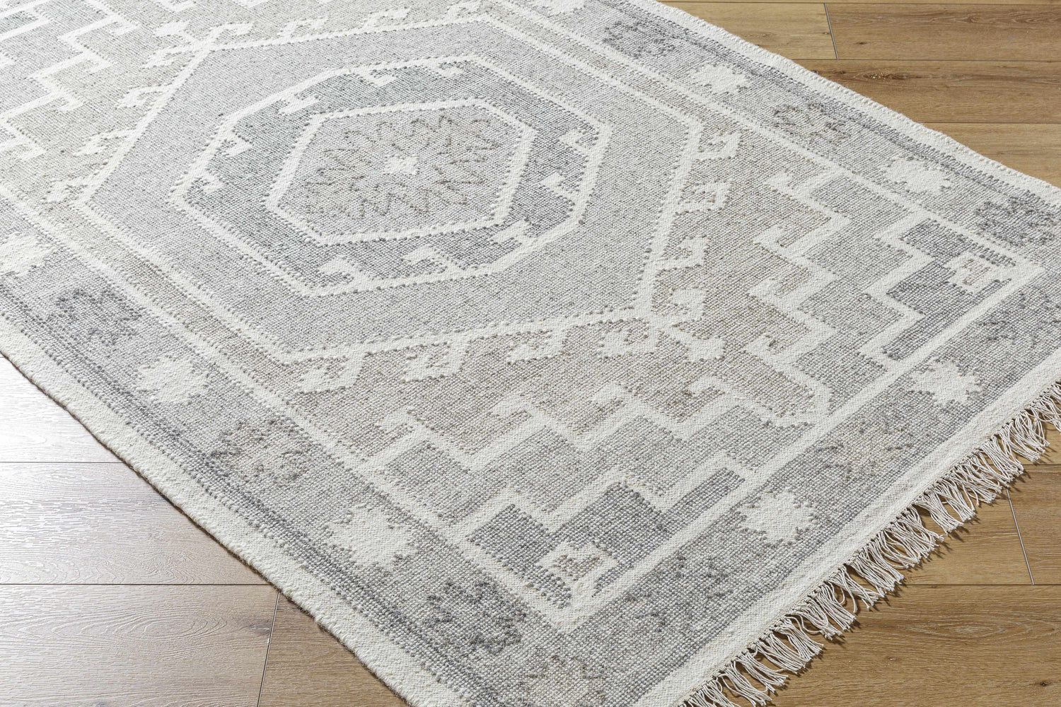 Close-up of the hand woven Donny Area Rug in beige and gray with a traditional geometric pattern and fringe. Corner