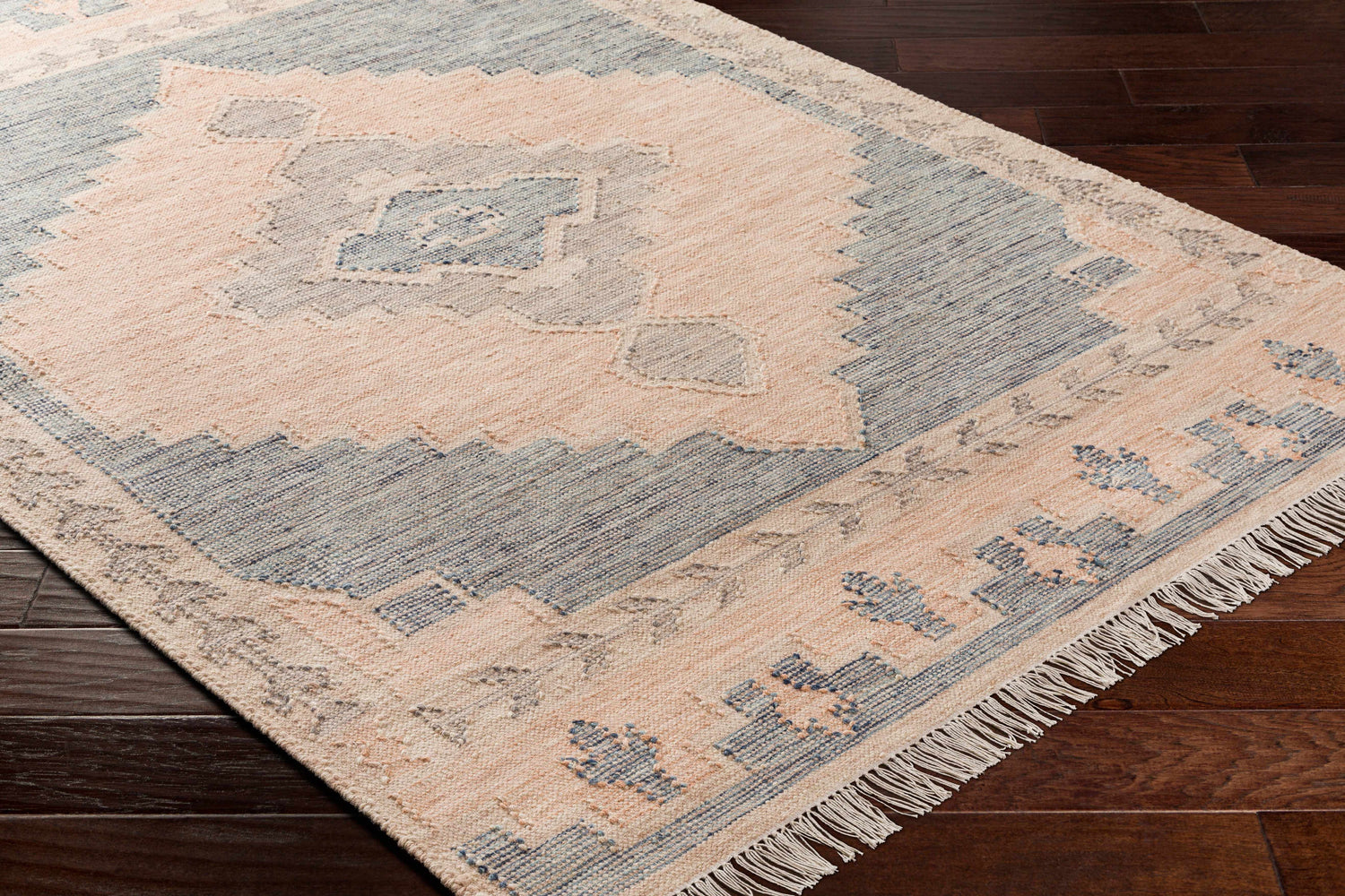 Close-up of the hand woven Lana Area Rug. Features a traditional geometric pattern in light brown and gray tones. Corner