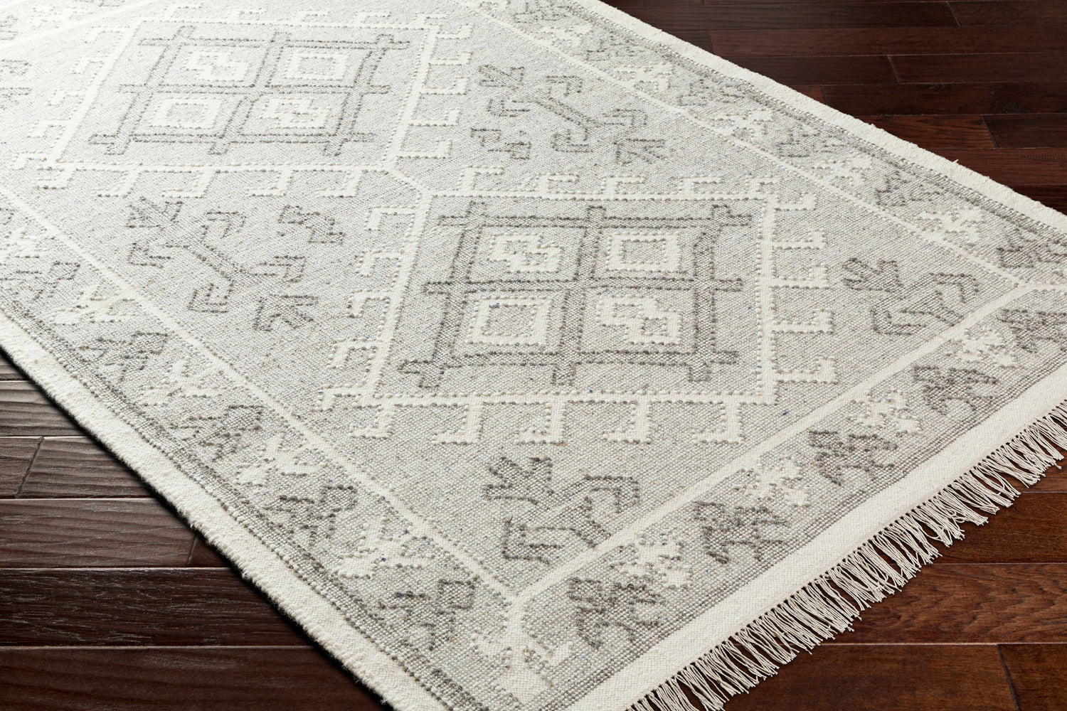 Close-up of the hand woven Memo Area Rug, a farmhouse style wool rug with gray geometric patterns on a dark wood floor. Corner
