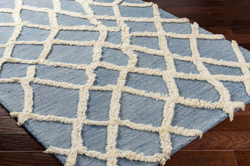 Close-up of Adica Blue Wool Area Rug showing geometric trellis pattern and soft, textured wool on dark wood floor. Corner