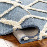 Close-up of the Adica Blue Wool Area Rug showing its texture and geometric ivory shag design on a wood floor. Fold