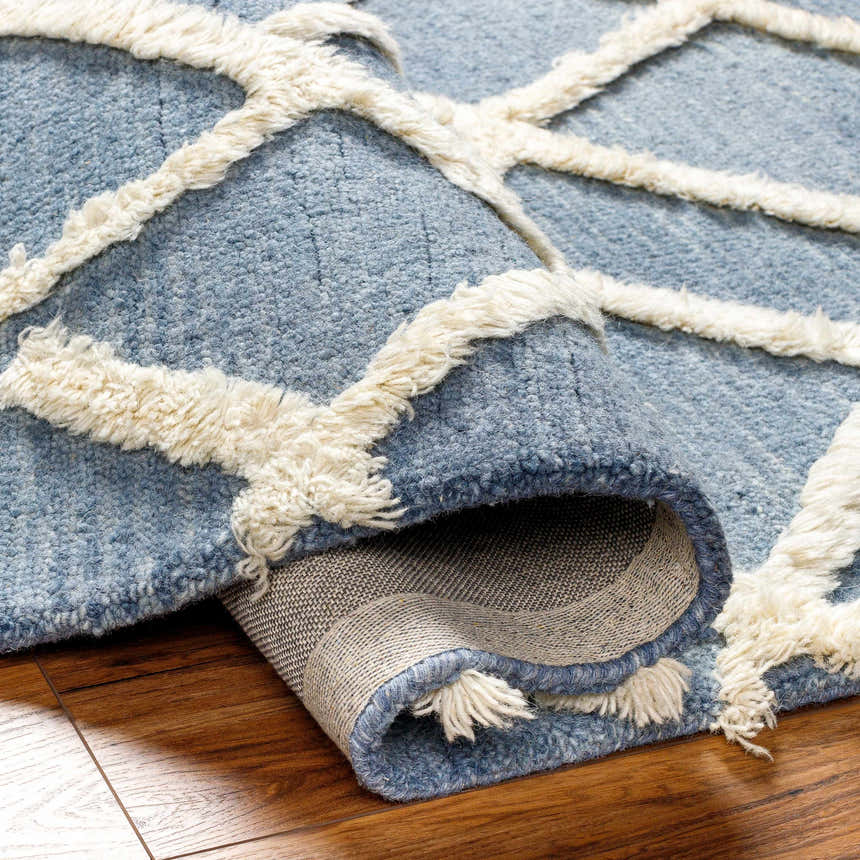 Close-up of the Adica Blue Wool Area Rug showing its texture and geometric ivory shag design on a wood floor. Fold