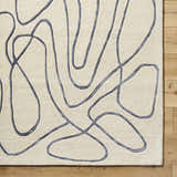 Close-up of the hand-tufted Derek Area Rug. Ivory rug with a contemporary dark gray abstract line pattern. Wool texture. Corner