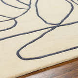 Close-up of the Derek Area Rug showing its dark gray abstract pattern on a light peach wool texture. Contemporary style. Texture