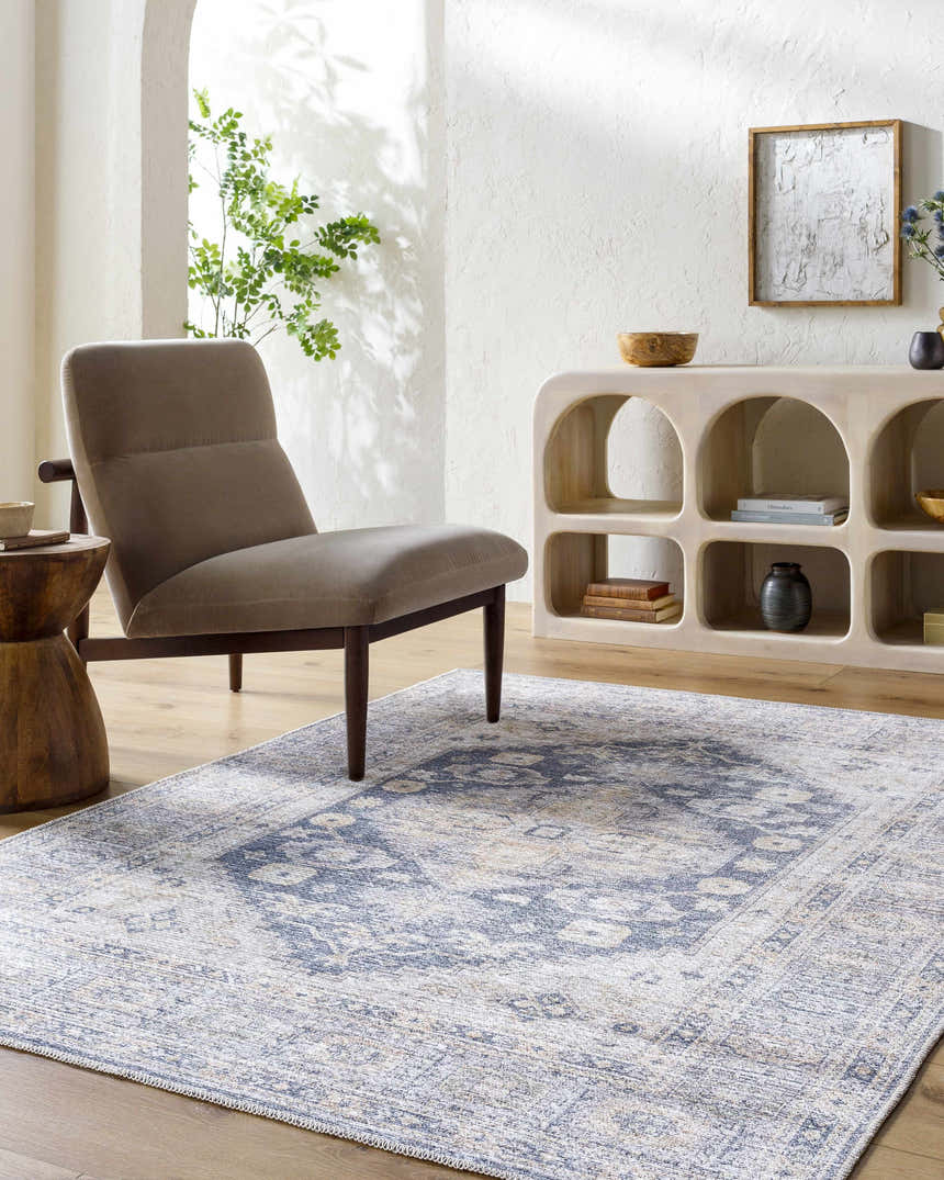 Living room scene with a blue and beige Keola Washable Area Rug, gray chair, and arched display cabinet. Roomscene-Rectangle